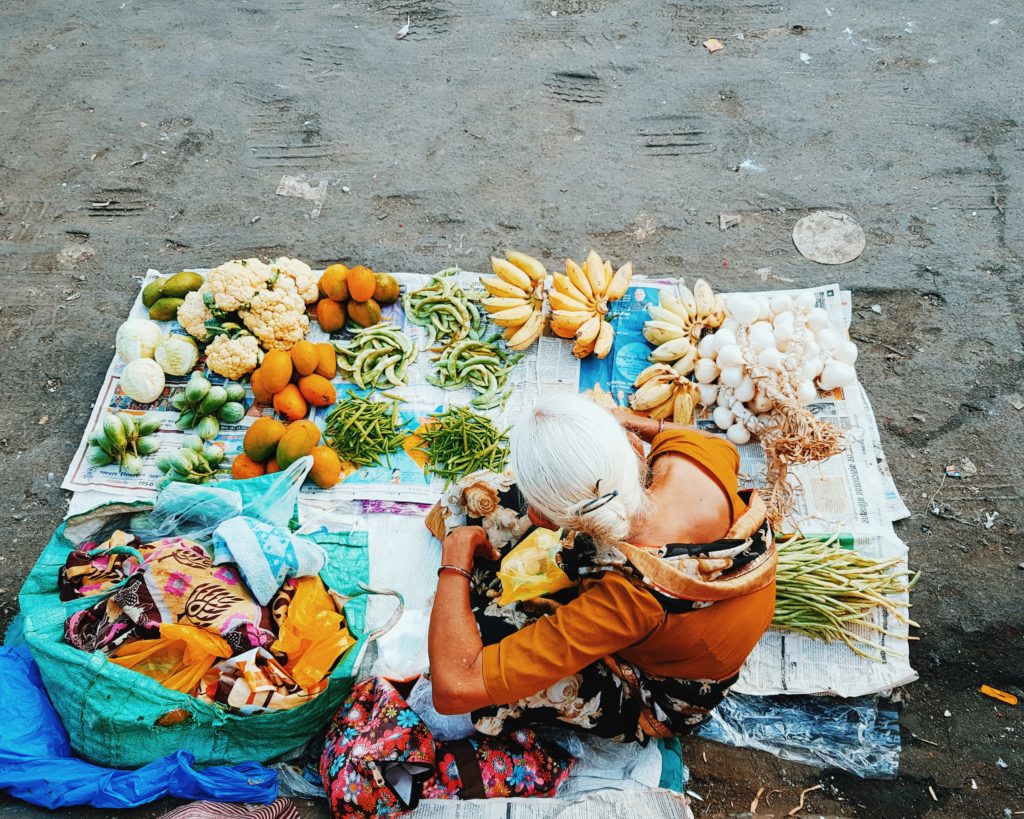 Person squatting on a mat, selling vegetables