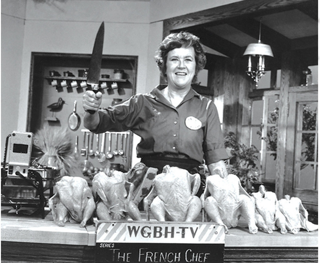 Black and white image of a person holding a large kitchen knife over a row of raw chickens