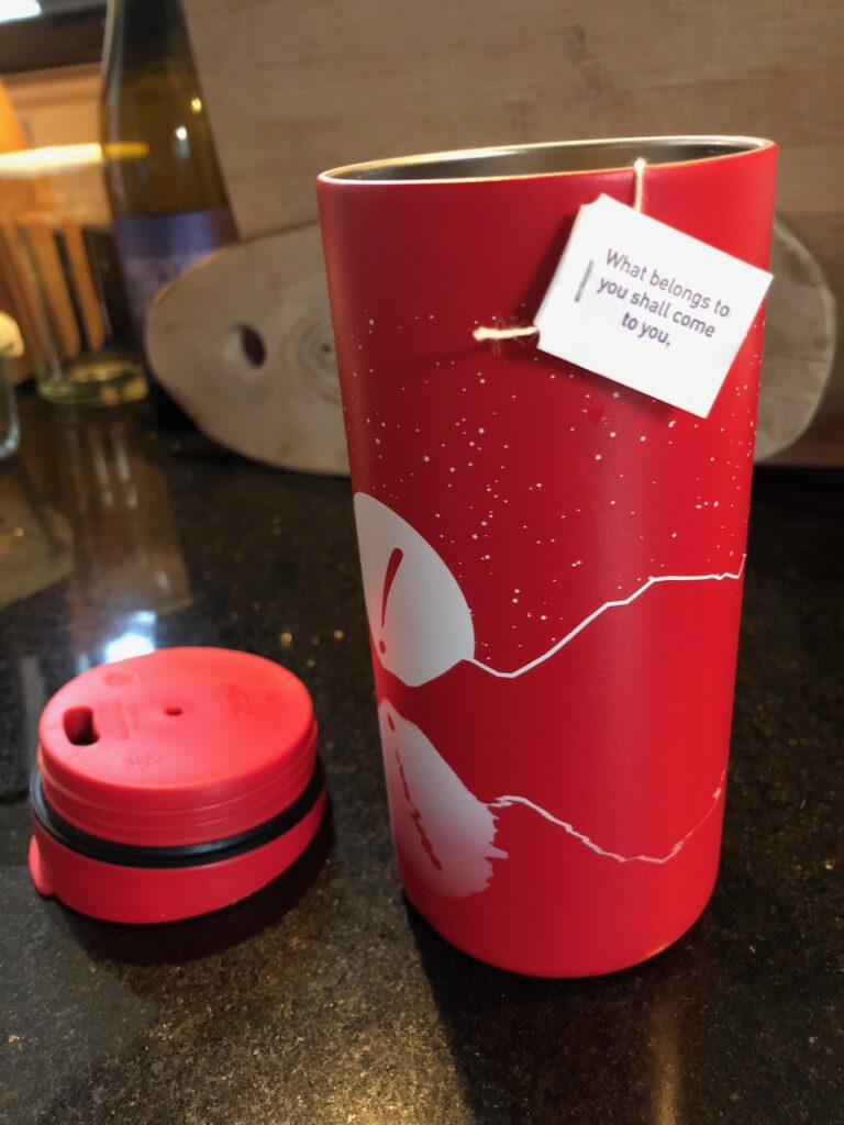 A red cylindrical metal container, with a tea bag draped over the top.