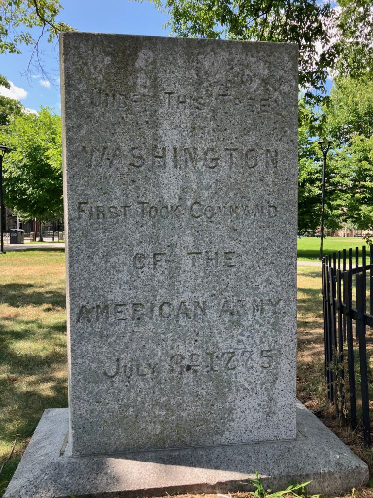 A very old stone monument, shaded, with a bright, sunny park behind it