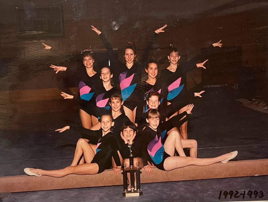 Ten young gymnasts pose as a team with their hands out