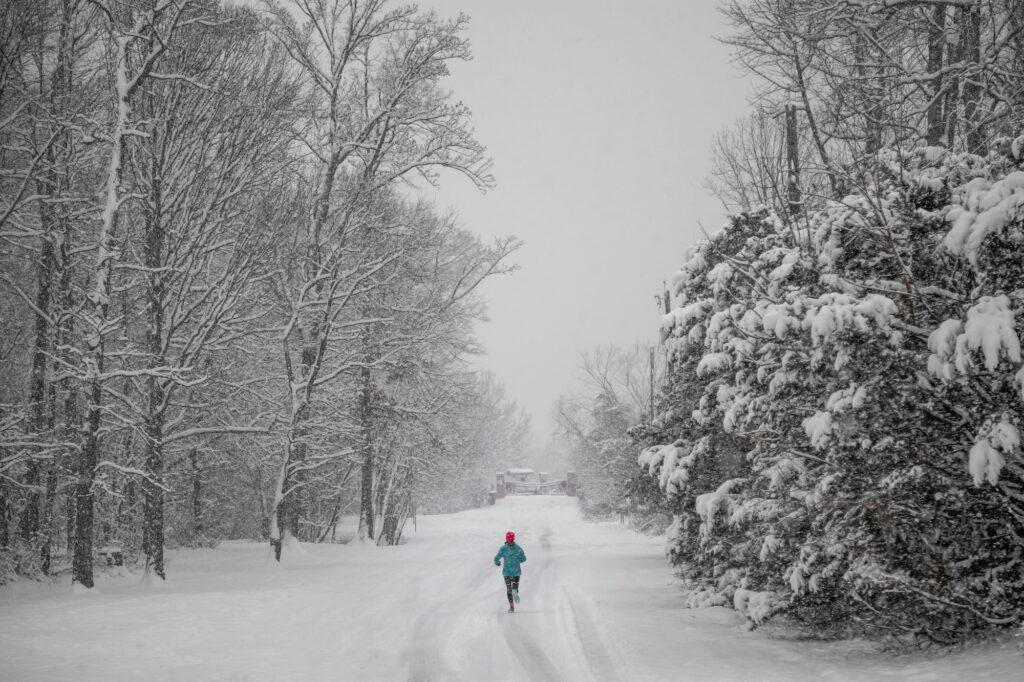 Person wearing blue jacket and red hat running on a snowy road