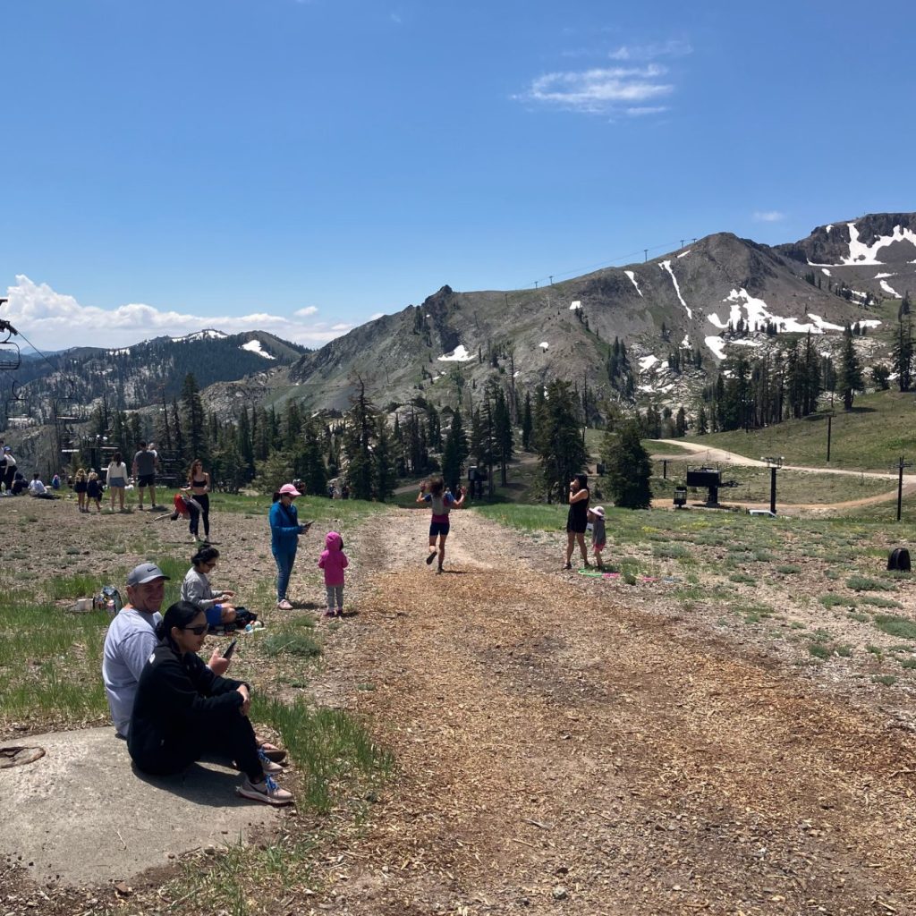 A road with a runner on it and people along the side of the road. mountain in the distance and blue sky